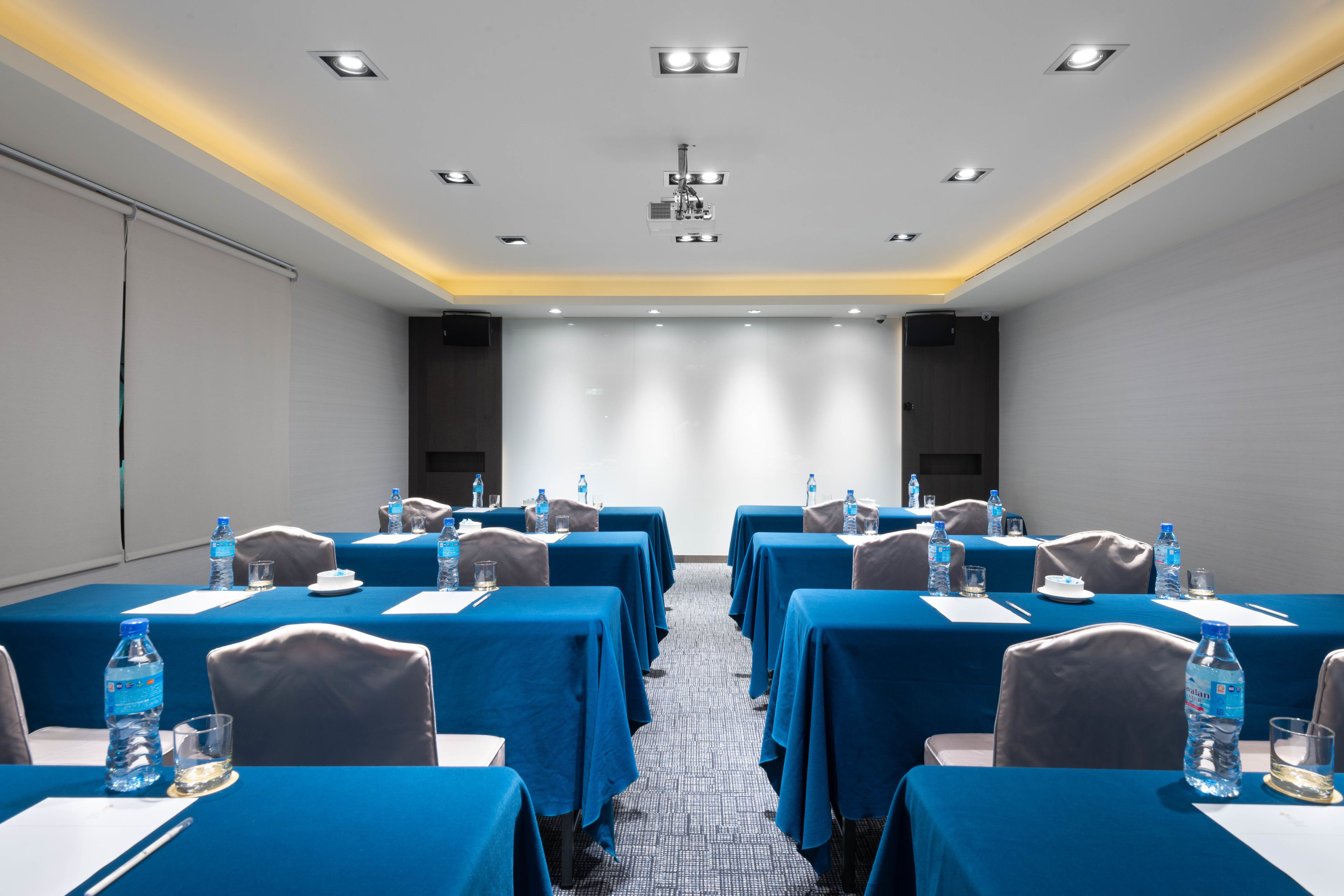 A conference room with multiple tables, each covered with a blue tablecloth, and equipped with water bottles and glasses.