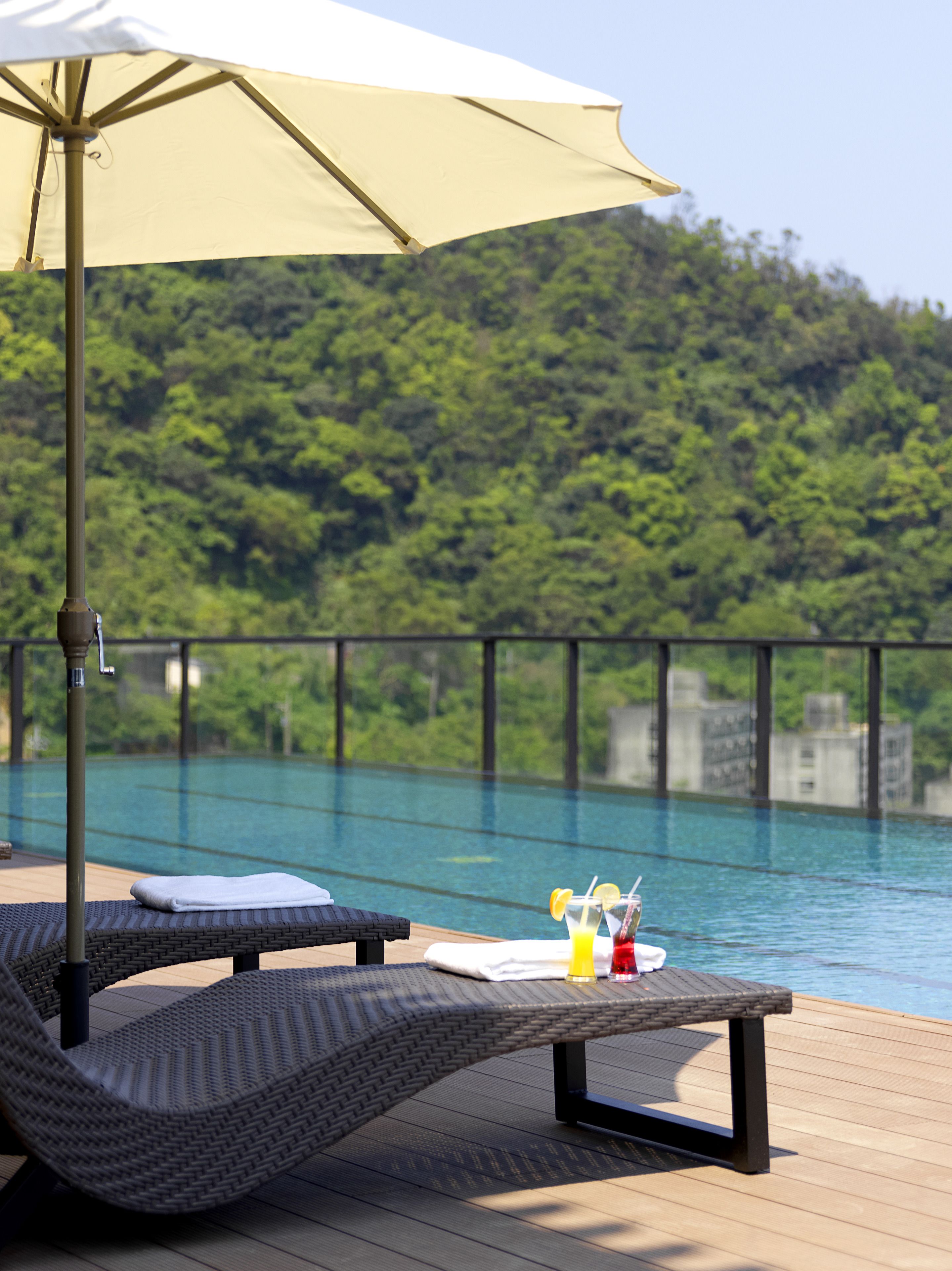 A poolside area with a lounge chair, a table with a drink, and an umbrella.