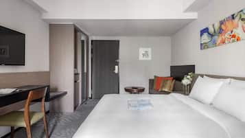 A hotel room with a bed, a desk, a chair, a TV, and a painting on the wall.