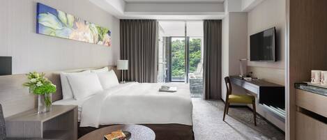 Habitación de hotel con cama, escritorio, televisión y vistas a zonas verdes.