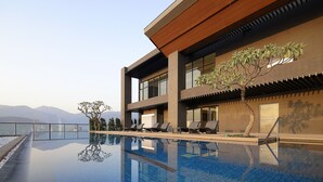Un edificio moderno con piscina infinita en la azotea, sillones de descanso y vistas a las montañas.