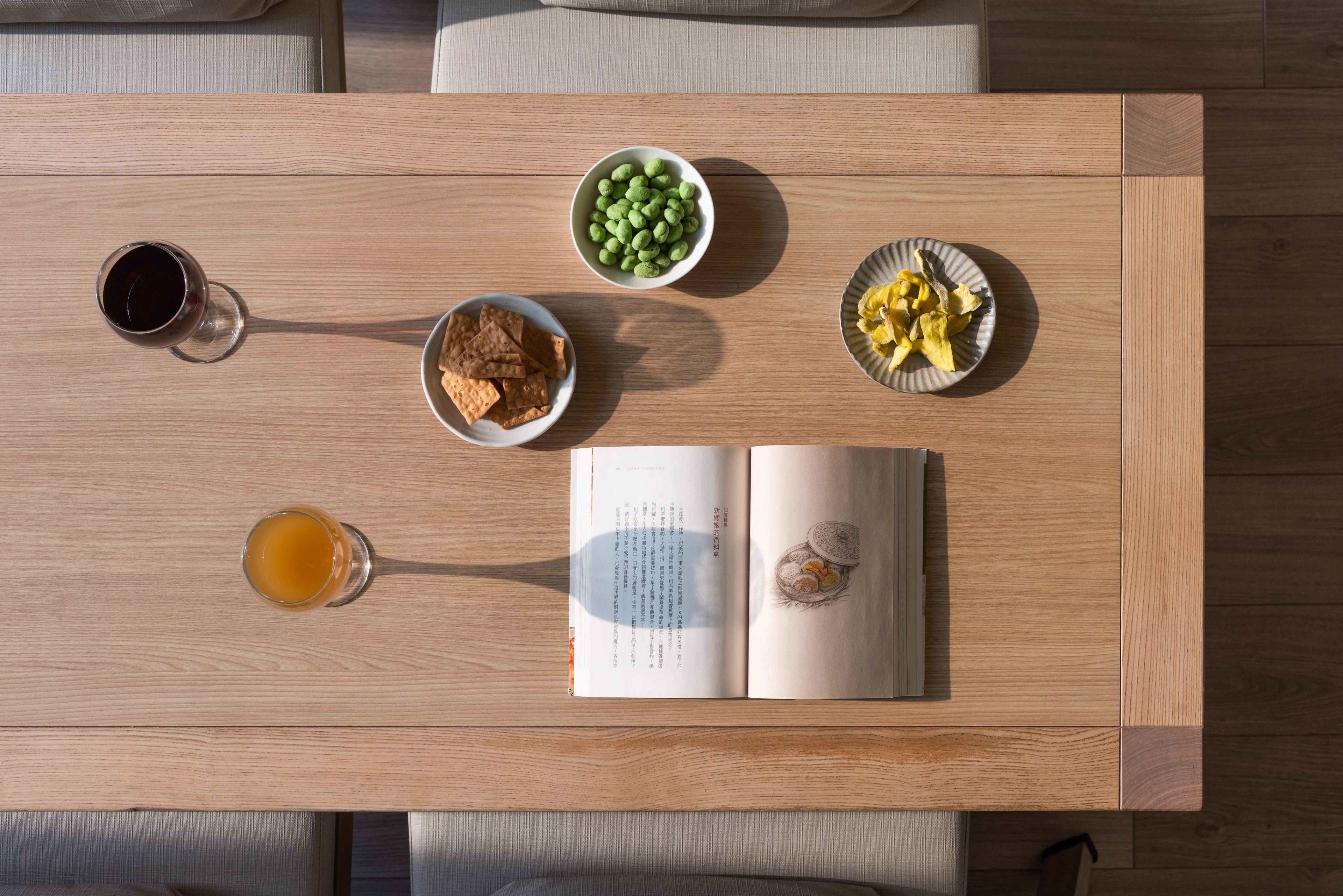A wooden table with a book, bowls of snacks, and glasses of juice.