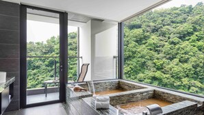 Un baño moderno con una bañera grande, ducha y vistas a un bosque frondoso.