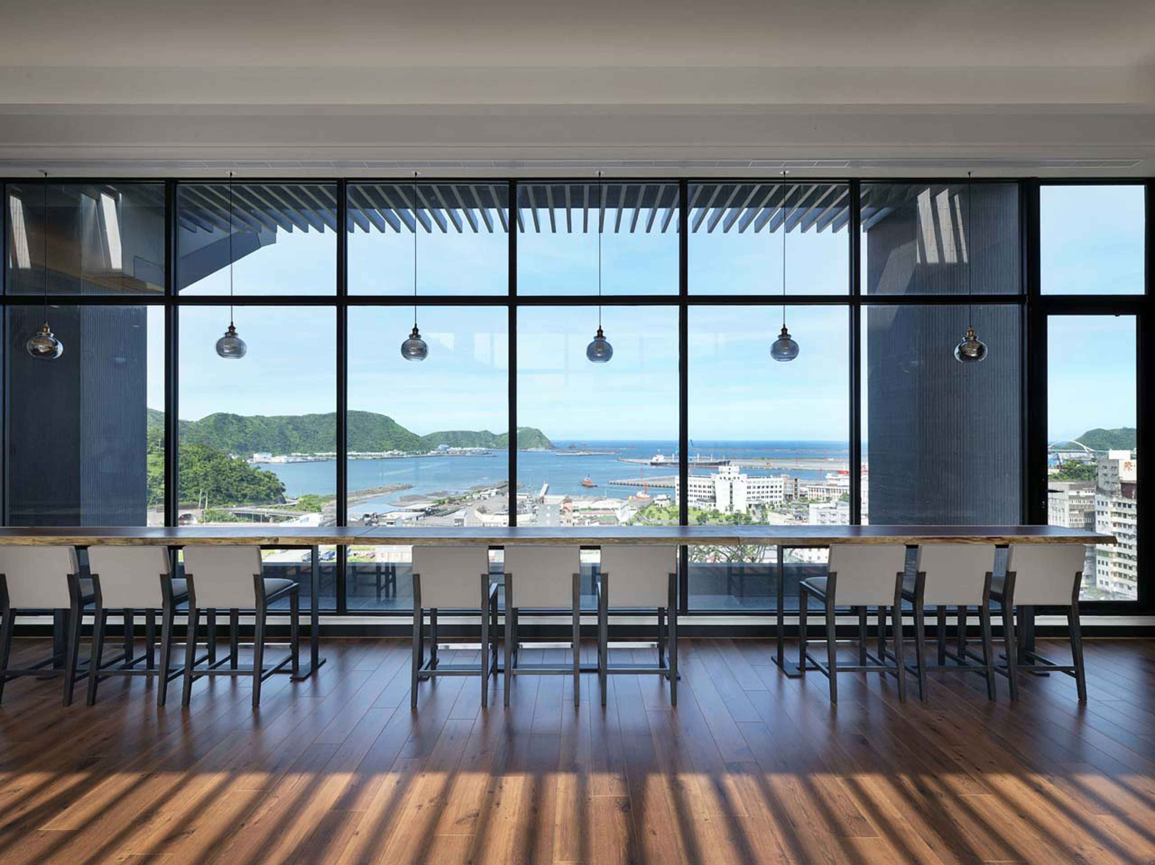 Una habitación amplia con ventanas grandes que ofrecen vistas a una ciudad costera.