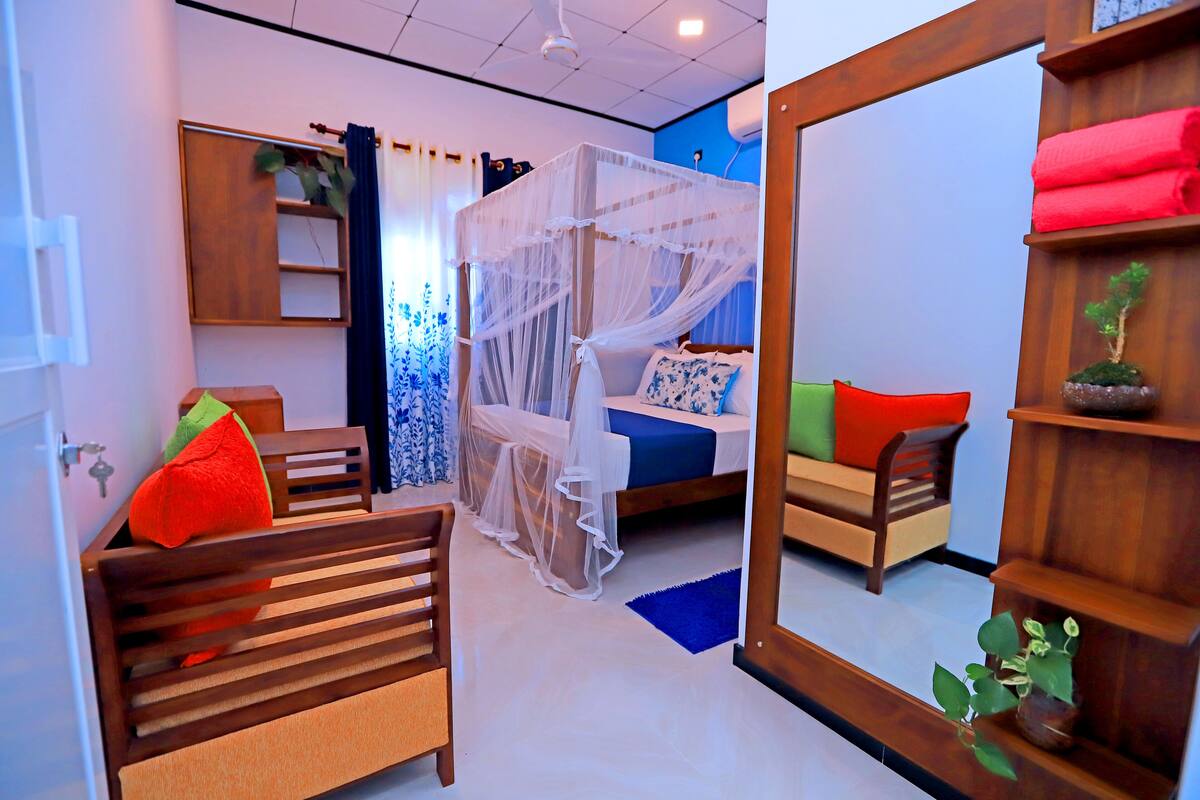 A bedroom with a bed, a wooden bench, a bedside table, a mirror, and a small plant.