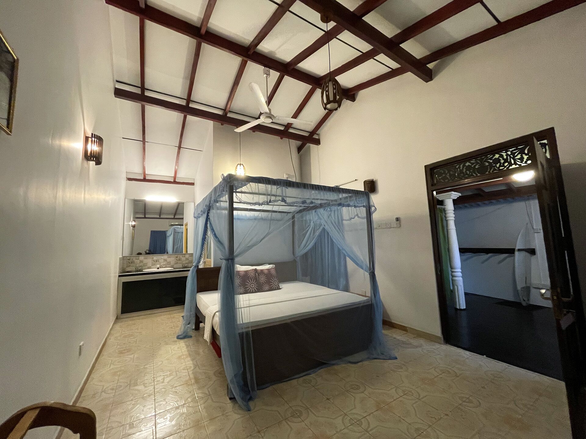 Un dormitorio con una cama con dosel, un ventilador de techo, un espejo y una puerta con marco decorativo.