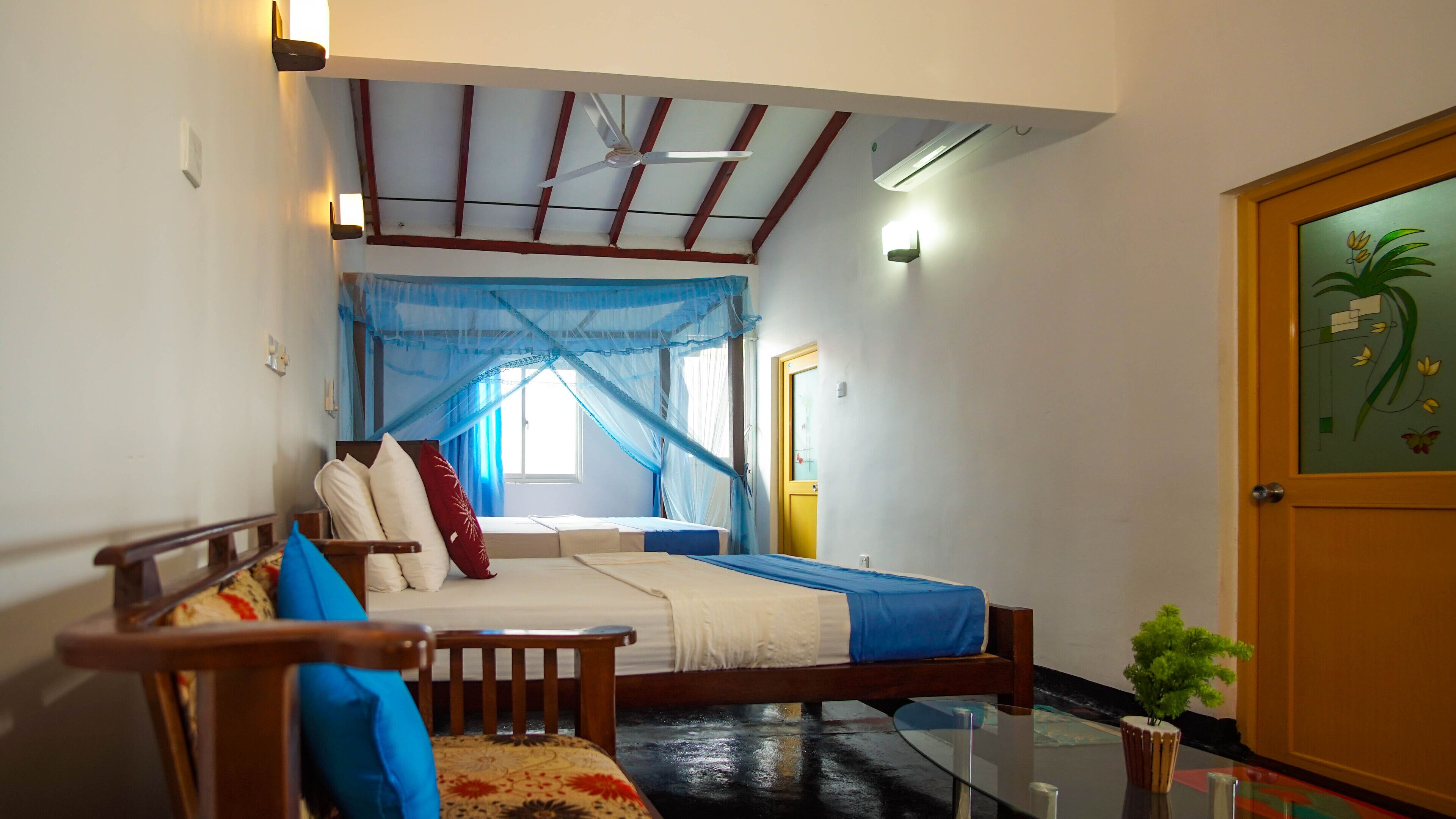 A room with a bed, a chair, a small table, a door with a decorative glass panel, and a ceiling fan.