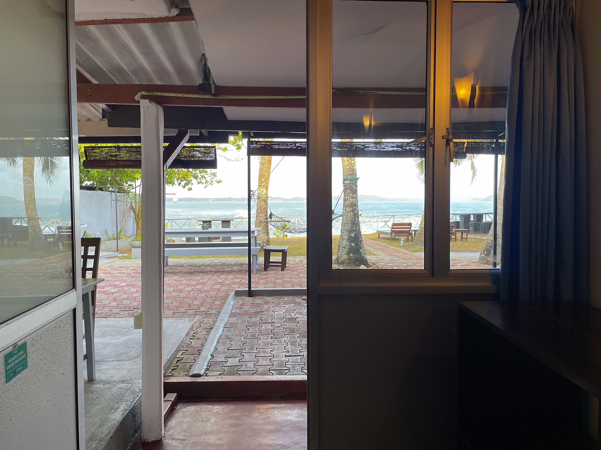 A room with a large window overlooking a beach area, a hammock, and a bench.