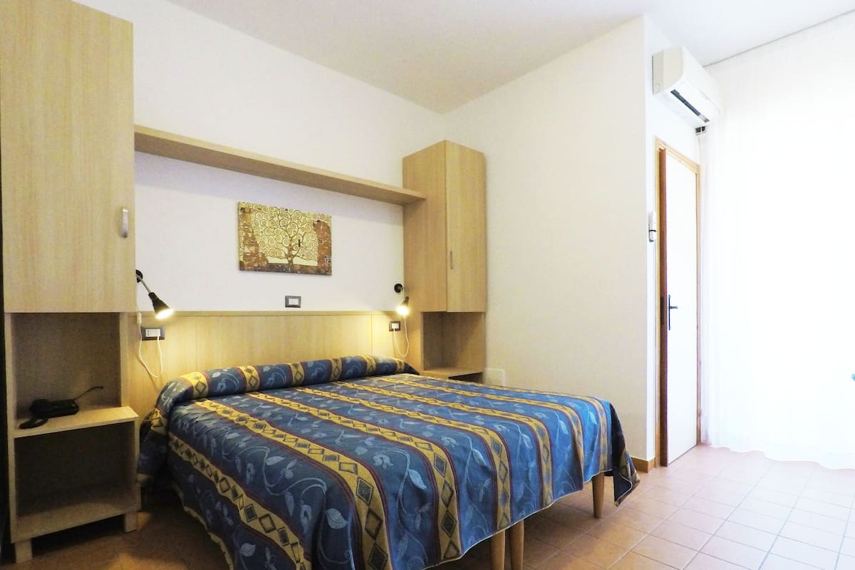 A bedroom with a bed, bedside tables, a wall-mounted lamp, and an air conditioning unit.