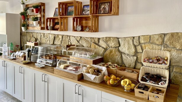 Ein Frühstücksbuffet mit verschiedenen Speisen, Holzeinlegeböden und einer Wand aus Stein im Hintergrund.