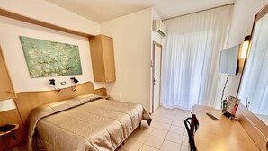 Ein Hotelzimmer mit Bett, Schreibtisch, Stuhl, einem Gemälde, einer Klimaanlage und einem Fenster mit Vorhängen.