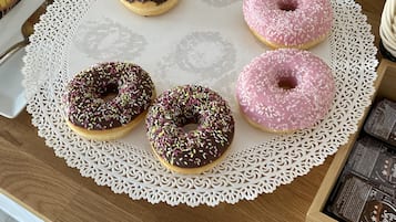 Una mesa de madera con un posavasos de encaje, cuatro rosquillas y una caja de barras de chocolate.