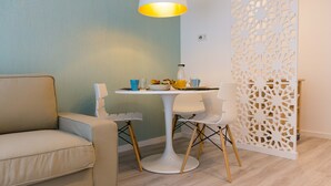 Uma sala de estar moderna com uma mesa branca redonda, duas cadeiras, um sofá bege e um painel branco decorativo com desenhos recortados detalhados.