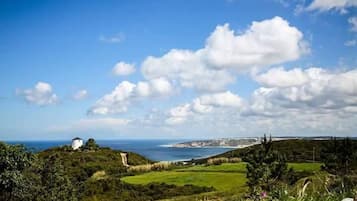 A coastal landscape with a white building on a hill, a clear sky, and a view of the sea.