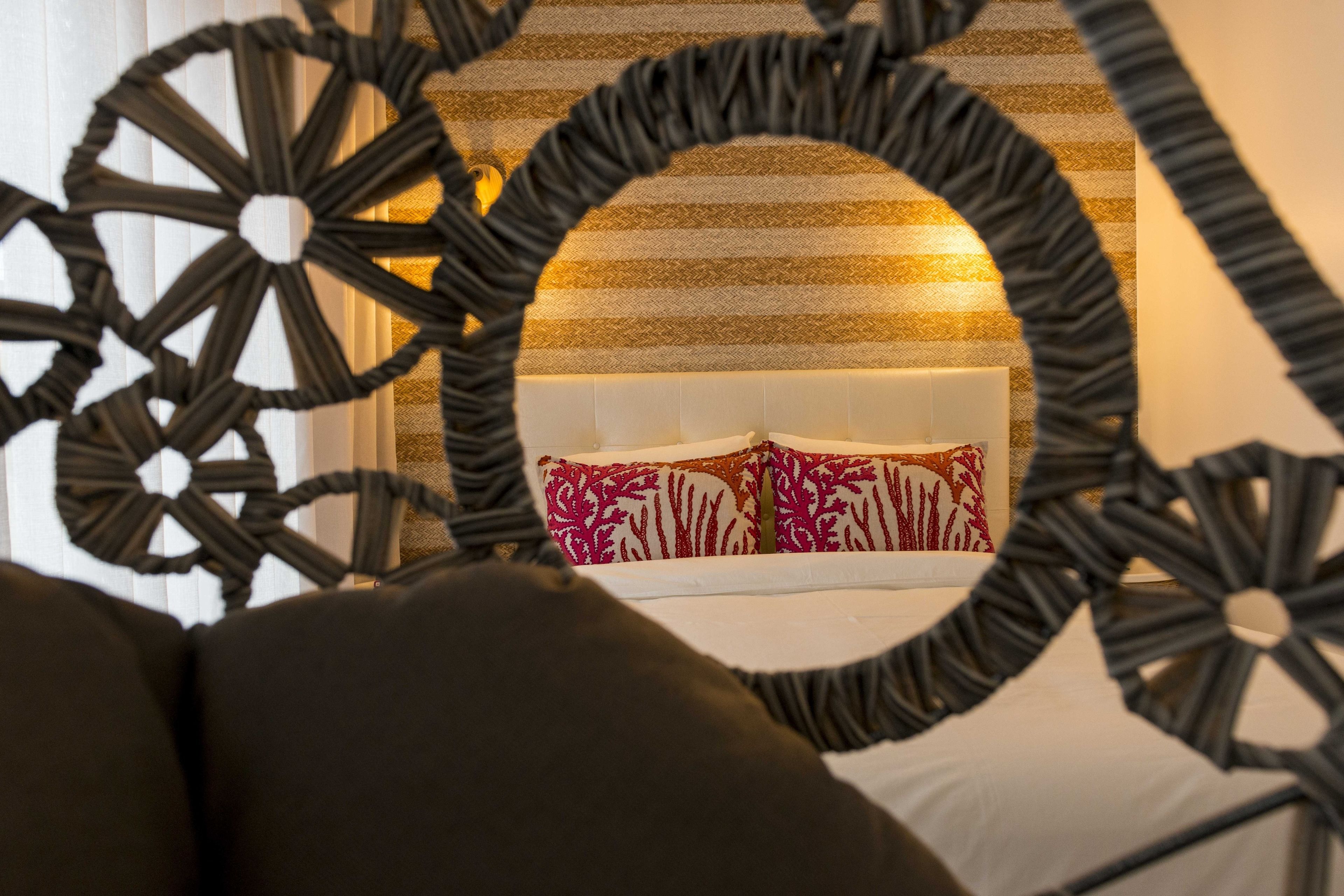 Una cama con cabecera blanca y almohadones estampados en rojo, enmarcada por un diseño circular negro decorativo.