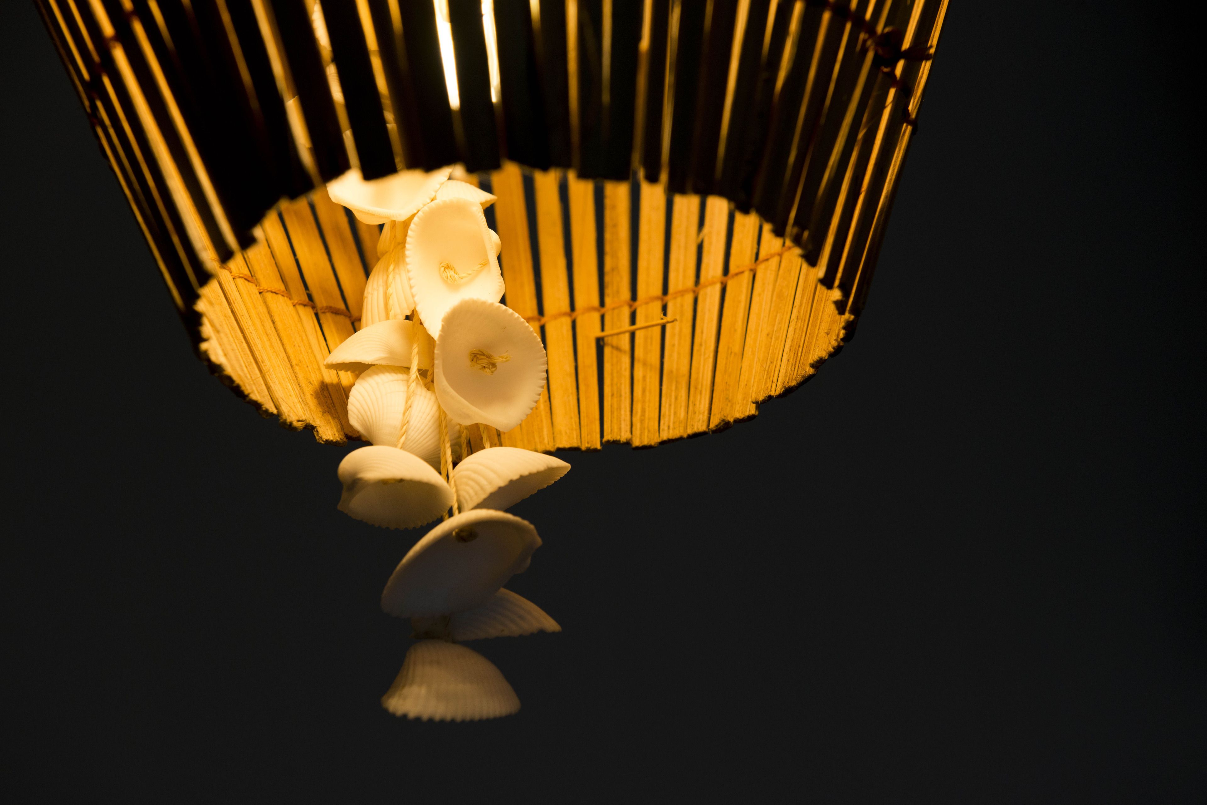 A hanging light fixture with a bamboo frame and white, scalloped-edged lampshades.