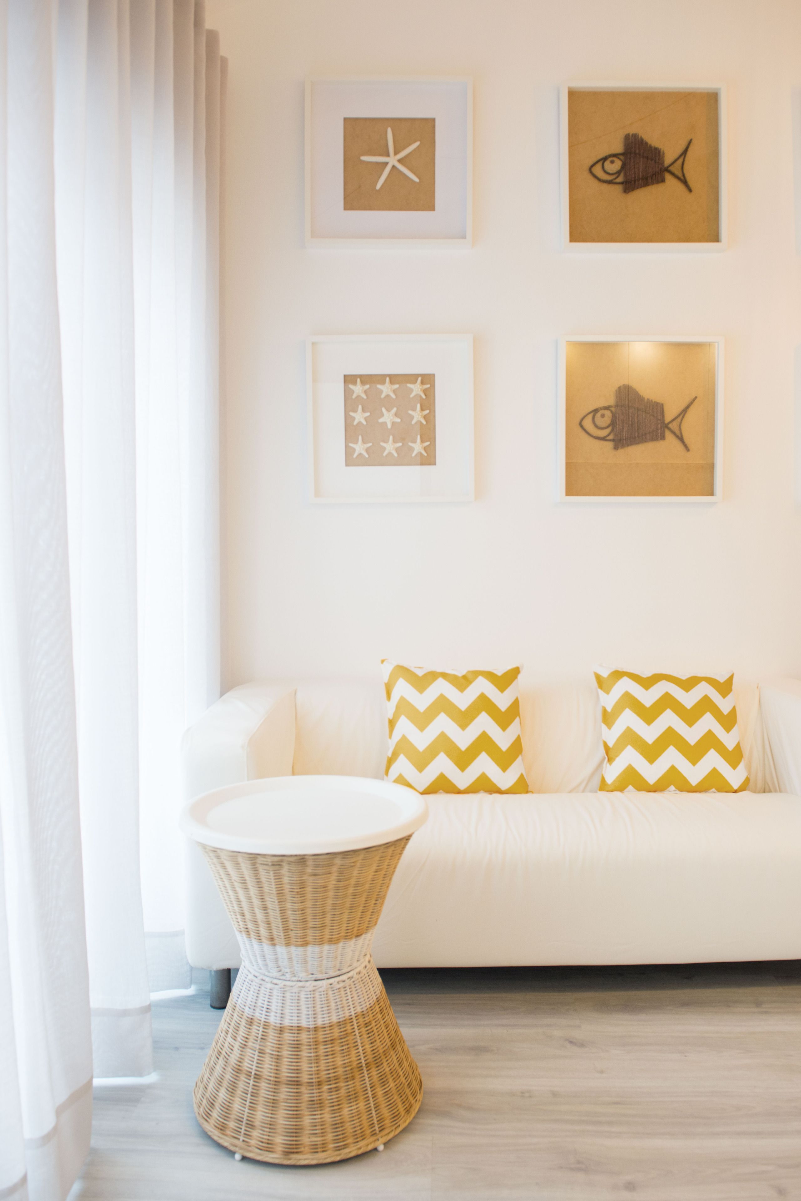 Un sofá blanco con dos almohadas de estampado en zigzag, una mesita de mimbre y cuadros en la pared.