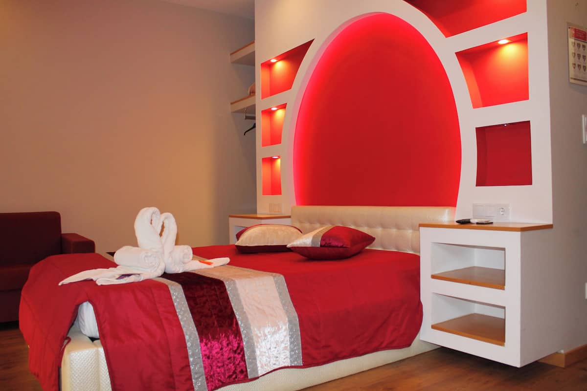 A modern bedroom with a red and white color scheme, a large bed, a bedside table, and built-in shelves.