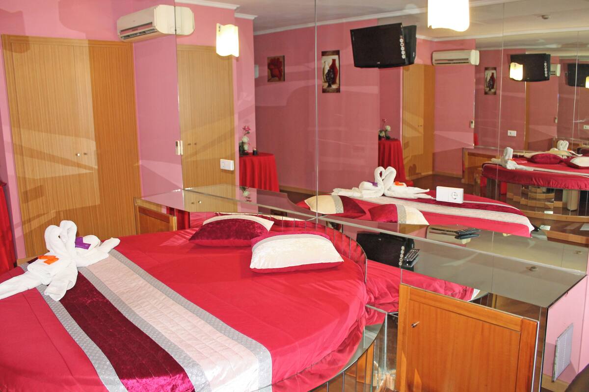 A hotel room with a large bed, a desk, a mirror, and a television.
