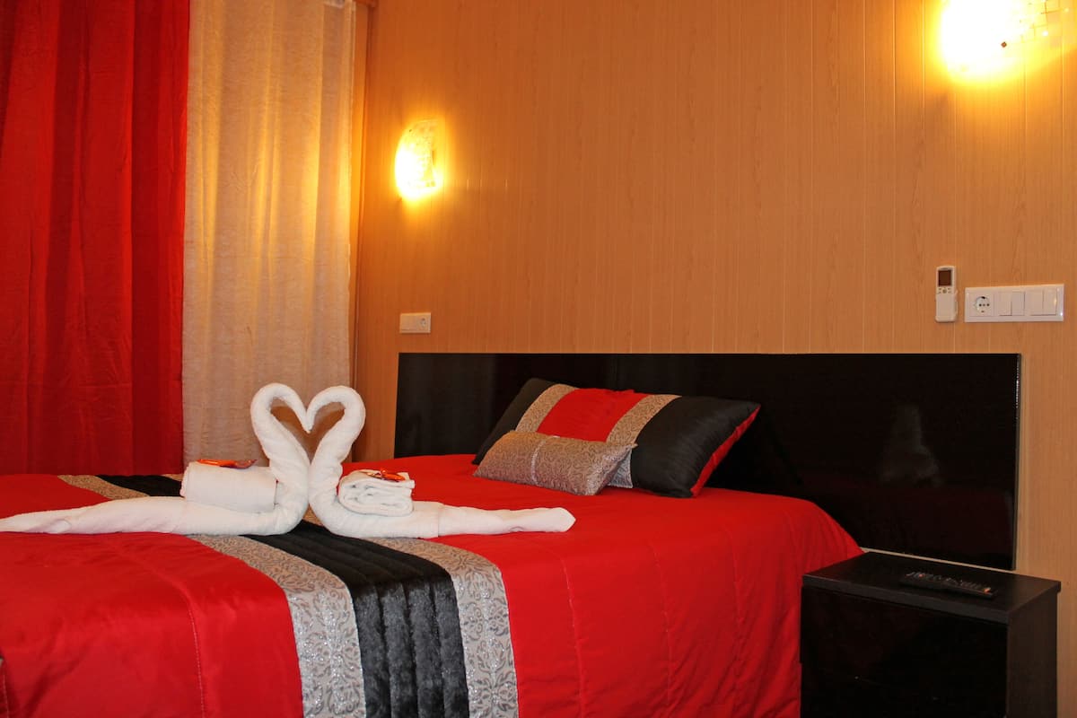 A hotel room with a red bedspread, a black headboard, and a wall-mounted light fixture.