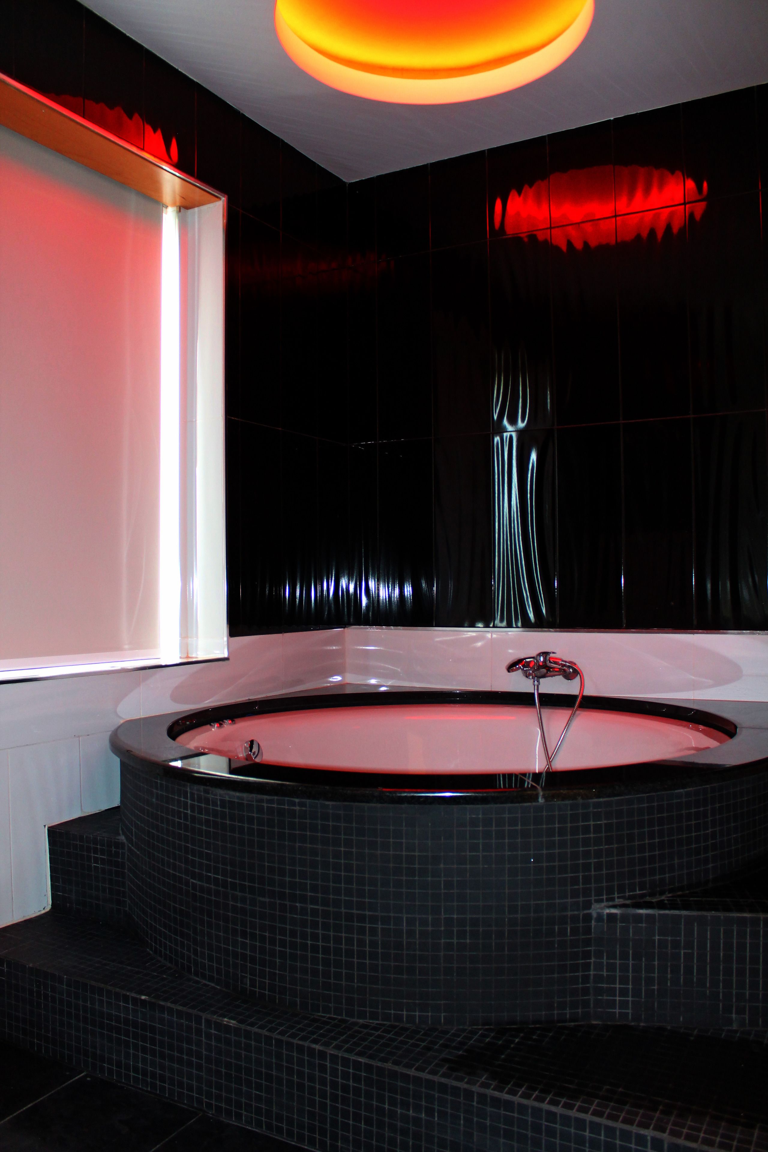Une salle de bain moderne avec une grande baignoire, des murs recouverts de carreaux foncés et un luminaire original.