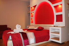 A modern hotel room with a red and white color scheme, a large bed with a headboard, a bedside table, and a built-in shelf unit.