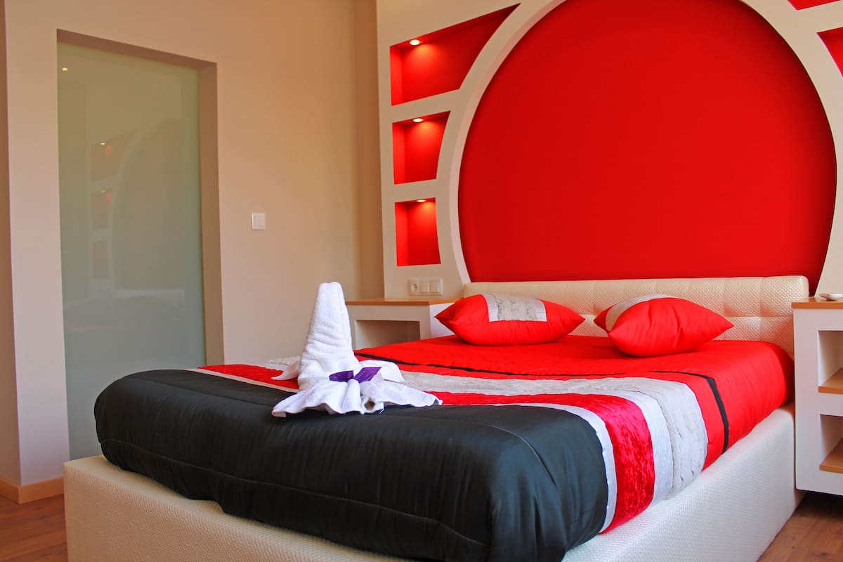 A hotel room with a large bed, red and black bedding, and a modern headboard with built-in lighting.
