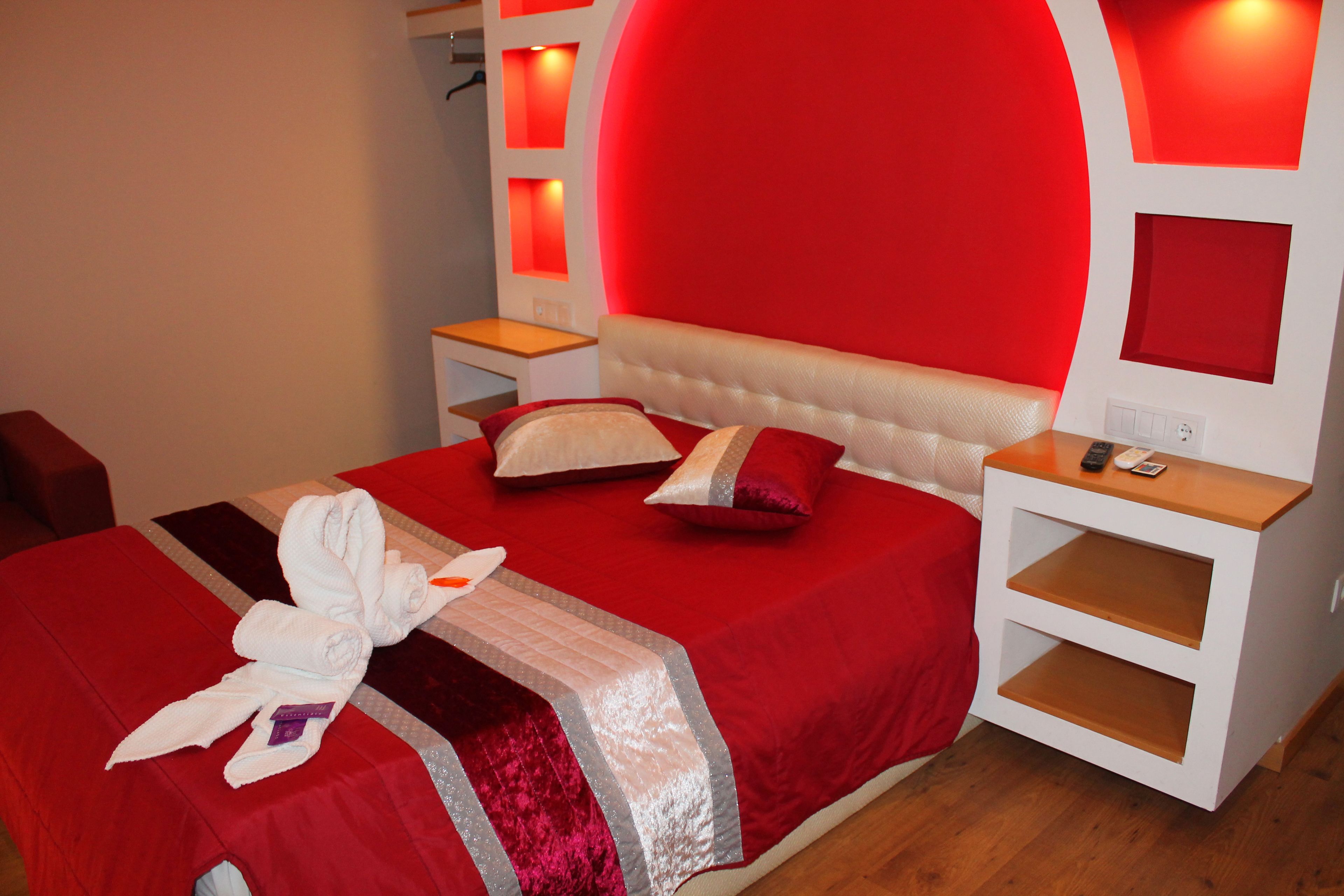 A hotel room with a red bedspread, a white headboard, and a red wall accent.