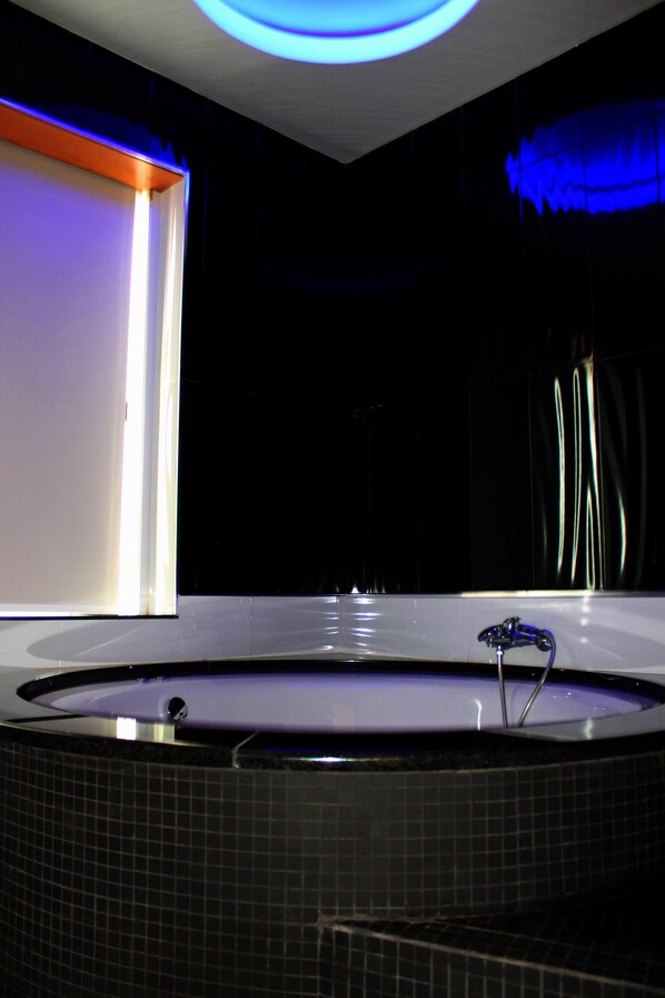 A modern bathroom with a bathtub, tiled walls, and a blue light fixture.