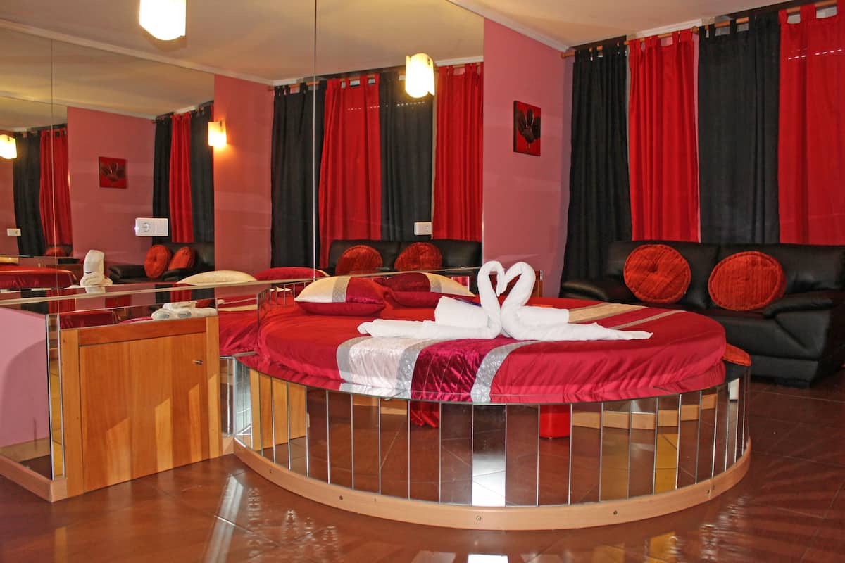 A circular bed with red bedding, a wooden side table, and a mirror.