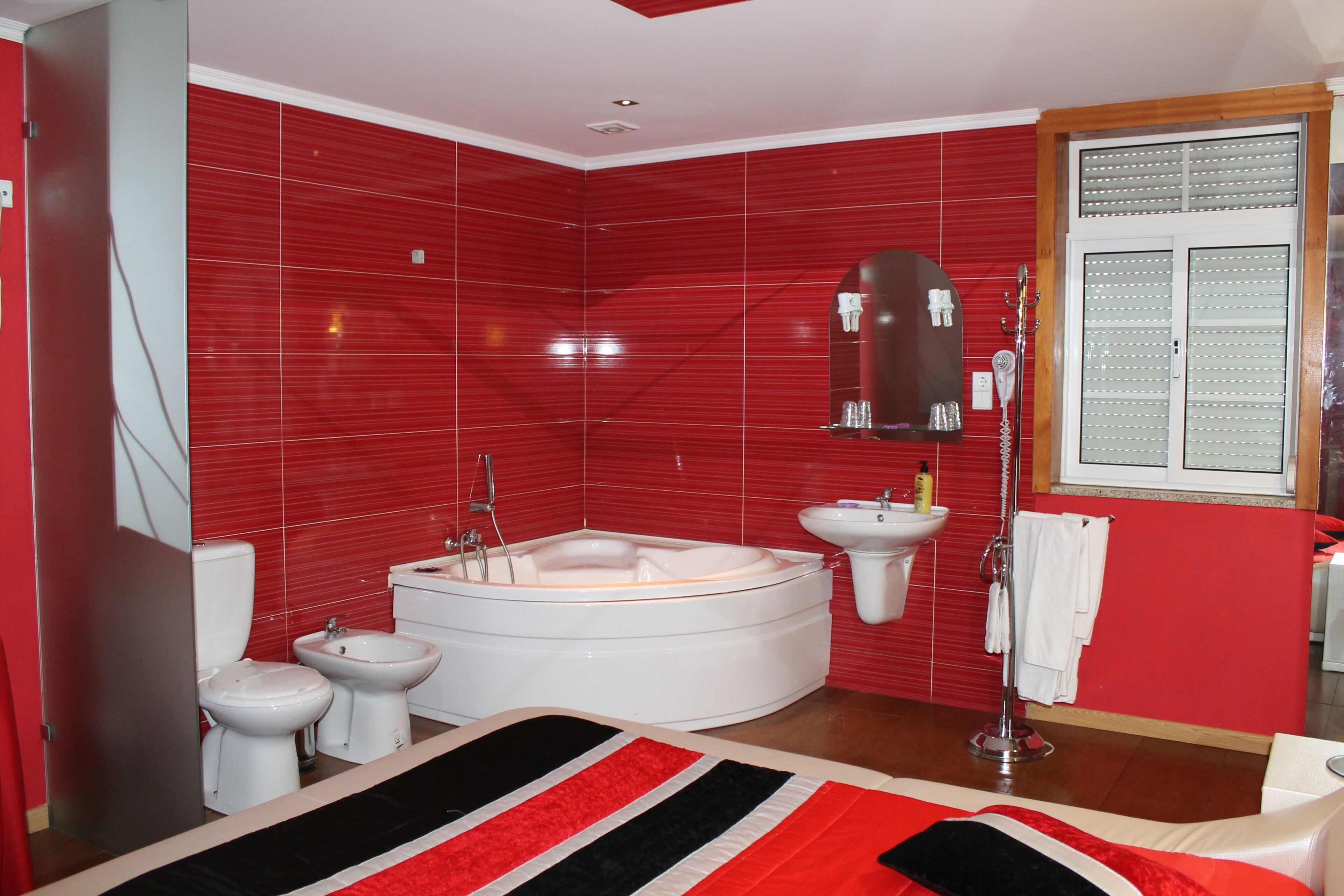 A modern bathroom with a red tiled wall, a large bathtub, a toilet, a bidet, and a sink.