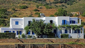 Un edificio blanco con contraventanas azules, un árbol en primer plano y una pared de piedra al frente.