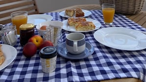 Una mesa dispuesta con alimentos para el desayuno, como pasteles, fruta y bebidas, con vista al mar de fondo.