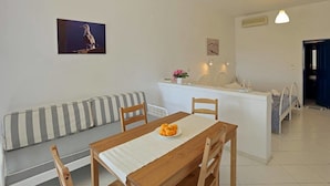 Un comedor con una mesa de madera, sillas y un banco. Hay una pequeña isla con un lavamanos y un florero con flores.