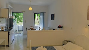 Habitación de hotel compacta con kitchenette, una cama con toallas, una mesita de noche pequeña y una ventana con vista a zonas verdes.