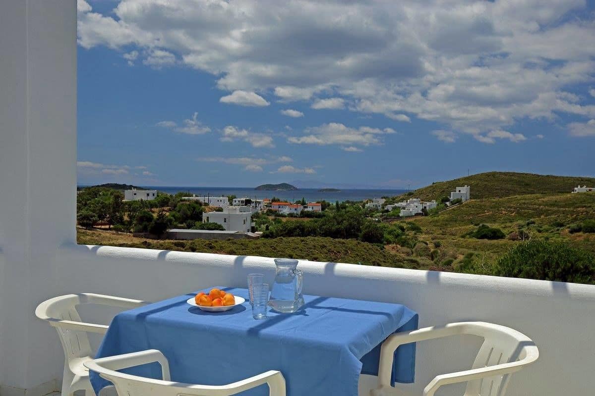 Un balcón con una mesa para dos, con vista a un paisaje costero con casas y colinas.