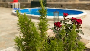 A swimming pool with a stone wall in the background, a red chair, and red flowers in the foreground. - Pelion Goddess Villas (Volos)