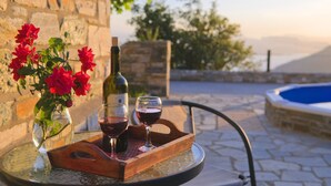 A table with a wine bottle, glasses, and a wooden tray on a glass table. - Pelion Goddess Villas (Volos)