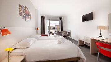 Habitación de hotel con dos camas, un escritorio, una silla, televisor y balcón con mesa y sillas.