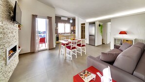 Uma sala de estar moderna com lareira, uma área de jantar e uma cozinha ao fundo.