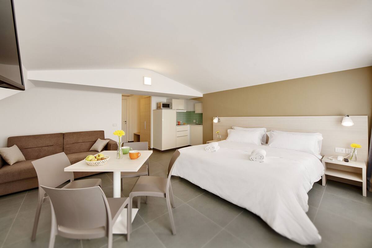 Ein modernes Hotelzimmer mit Bett, Sofa, Esstisch und einer Küchenzeile.