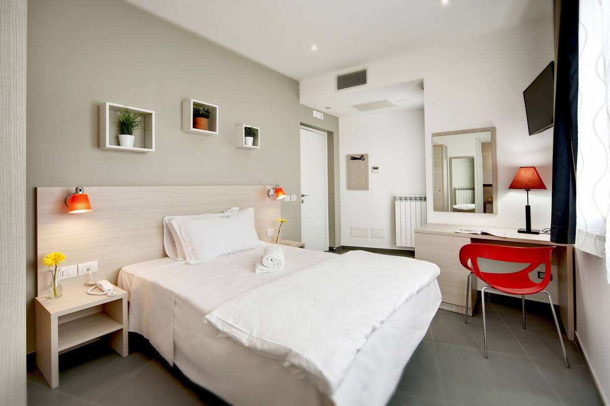 Ein Hotelzimmer mit Bett, Nachttisch, Lampe, Schreibtisch, Stuhl und Fernseher.