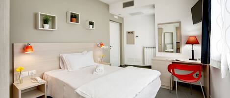 A hotel room with a bed, bedside table, lamp, desk, chair, and a TV.