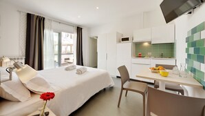 Quarto de hotel com cama, escrivaninha com cadeira, televisão, cozinha e vista para o exterior.
