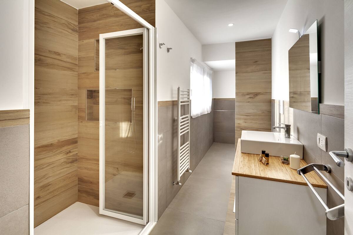 Ein modernes Badezimmer mit einer Duschkabine aus Holz, einem Waschtisch mit Spiegel und einem Handtuchhalter.