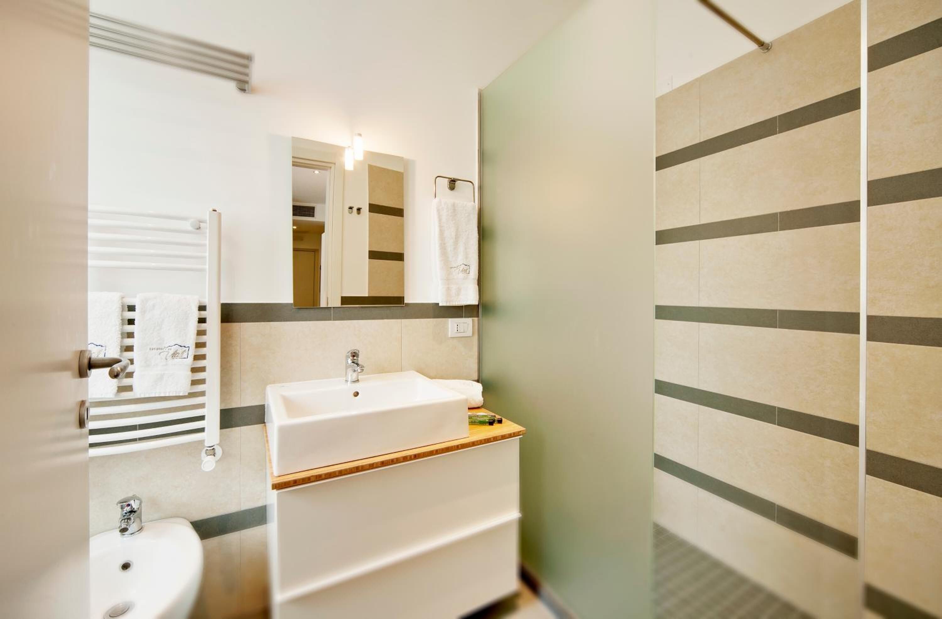 Un baño con lavamanos, espejo, toallero y azulejos rayados en la pared.