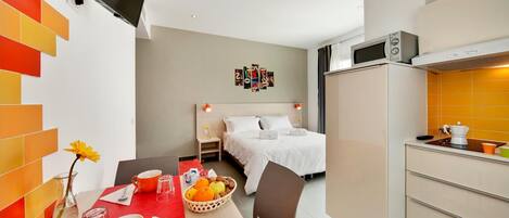 Habitación de hotel compacta con cama, kitchenette pequeña, zona de comedor con mesa y barra de desayuno.