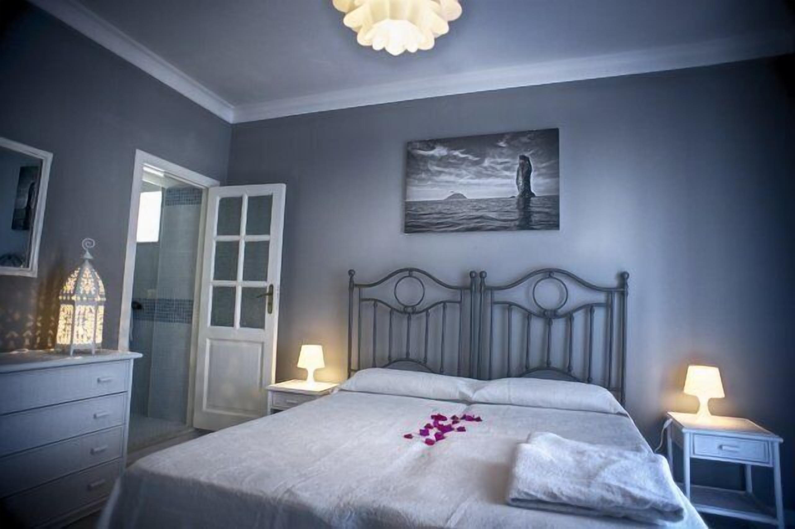Un dormitorio con cama, lámparas de noche, una puerta y un cuadro en la pared.