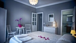 A bedroom with a bed, two chairs, a small table with flowers, a dresser, a mirror, and a ceiling light fixture. - B&B Il Cappero (Lipari)
