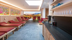 Un área de spa con bancos de madera, sillas rojas, un mostrador de recepción y vistas a las montañas a través de grandes ventanales.